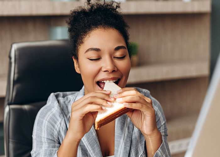 Young woman in casual wear eating a sandwich indoors, reflecting on terrifying close calls she will never forget.