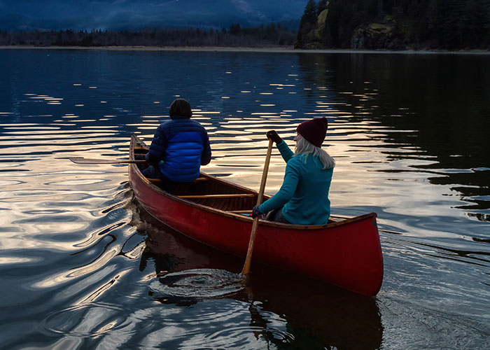Two people in warm clothing paddling a red canoe on calm water at dusk, capturing a close call moment outdoors.