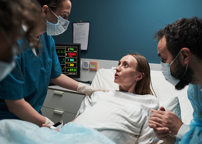 Female patient in hospital bed having a terrifying close call while medical staff and a visitor provide support.