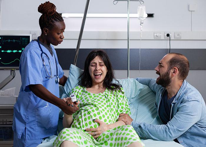 Pregnant woman experiencing a close call in hospital labor room with nurse and partner providing support during delivery.