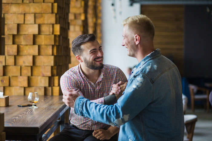 Two men laughing and shaking hands in a bar, illustrating high school bully reunion and karma moments.
