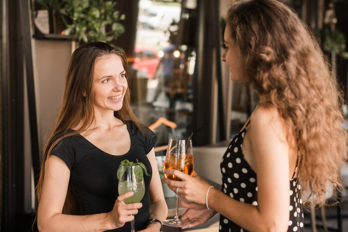 Two women meeting and talking over drinks, illustrating people meeting their high school bully as adults and karma.