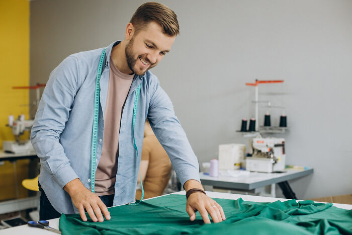 Man measuring green fabric in a workshop, smiling while working, illustrating positive change after high school bully encounters.