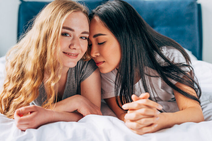 Two women lying on a bed smiling, representing people meeting their high school bully as adults and karma moments.