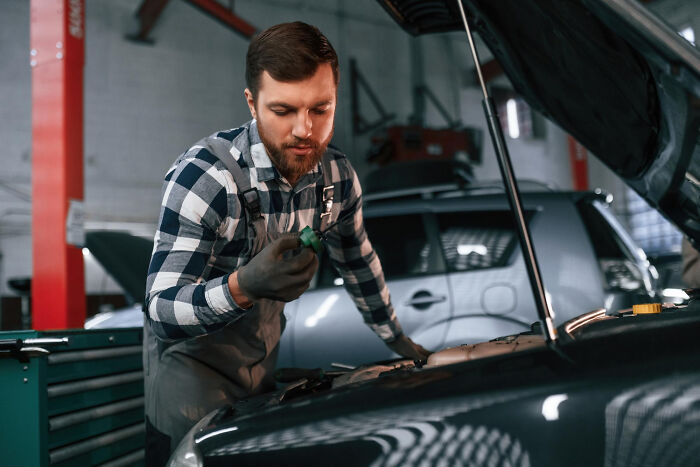 Man in plaid shirt and gloves fixing car engine, symbolizing karma moments when people met their high school bully as adults.