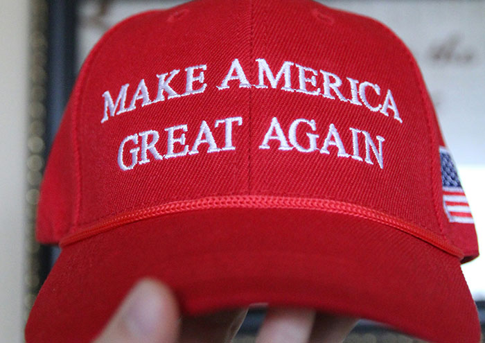 Red Make America Great Again hat with embroidered text and a small American flag on the side held close to the camera.