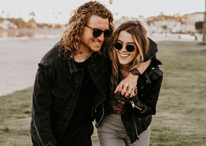 Young couple wearing sunglasses and leather jackets smiling and holding hands outdoors sharing explosive secrets anonymously.