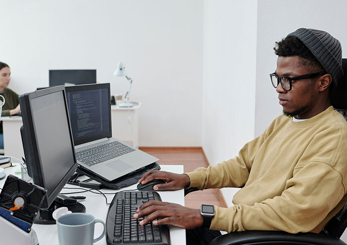 Man in a beanie and glasses typing on a keyboard, representing people anonymously sharing explosive secrets online.