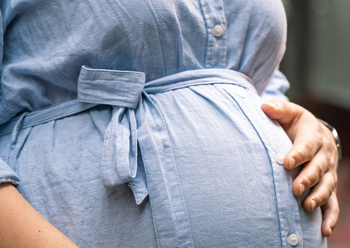 Close-up of a person in a blue shirt holding their pregnant belly, symbolizing anonymous secrets too explosive to expose.