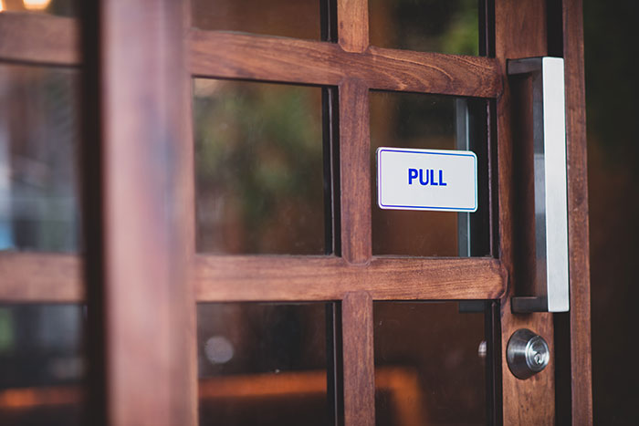 Wooden door with glass panels and a metal handle featuring a pull sign, symbolizing security guards reviewing camera footage.