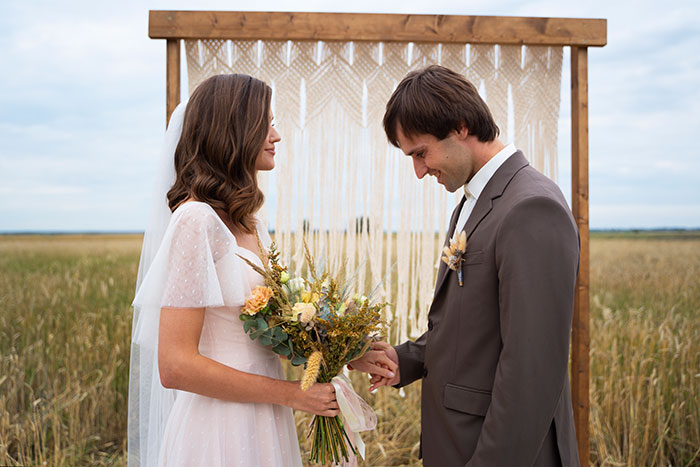 Bride holding bouquet facing groom in a field, illustrating tension with hubs relatives living with them and refusing to house his mommy.