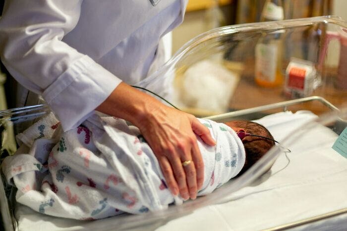 Doctor in a white coat handling a newborn in a hospital bassinet, illustrating unethical doctor actions with patients.