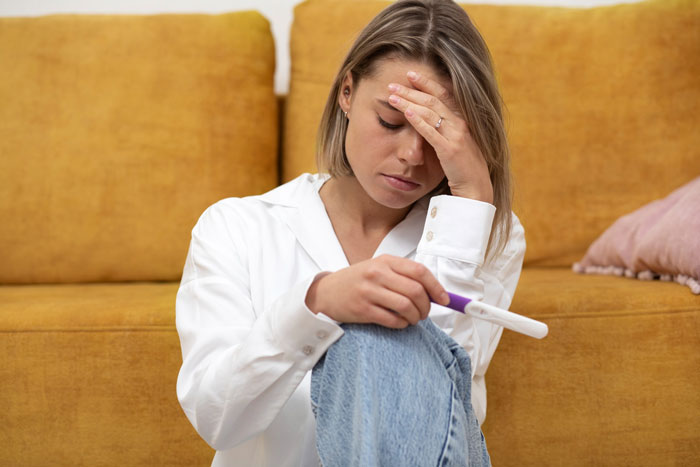 Young woman holding pregnancy test, looking stressed while sitting on the floor in a living situation setting