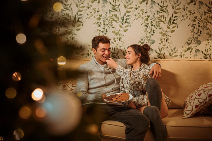 Young couple sharing cookies on a couch, illustrating a son and girlfriend relationship after high school advice conflict.