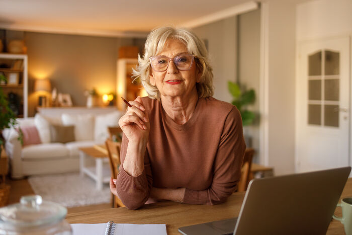 Older woman smiling thoughtfully at home, symbolizing mom inviting son's girlfriend to dad's party and his surprised reaction. Older woman smiling thoughtfully at home, symbolizing mom inviting son's girlfriend to dad's party and his surprised reaction.