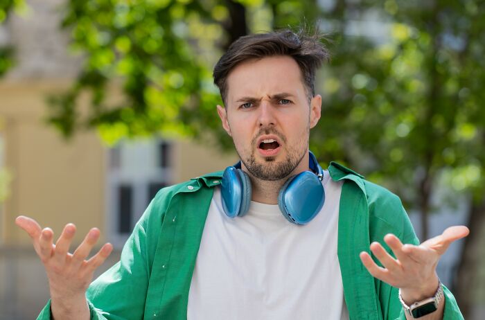 Young man with headphones around neck, looking confused and frustrated outdoors, reacting to rushed proposal at party