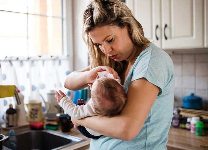 Woman caring for baby in kitchen, expressing frustration about cleaning and household responsibilities at home. Woman caring for baby in kitchen, expressing frustration about cleaning and household responsibilities at home.