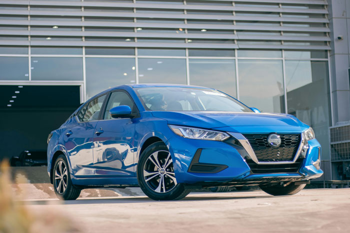 Blue sedan parked outside modern building, representing teen&rsquo;s first car as a debt trap and $40k loan repayment story.
