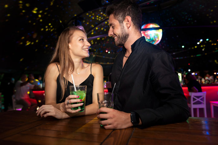 A strange guy and woman enjoying drinks together, smiling and chatting in a dimly lit relationship bar setting.