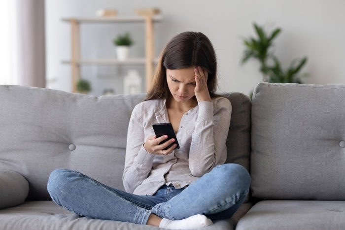 Young woman sitting on a couch looking stressed while using her phone, reflecting strange guy relationship bar feelings.