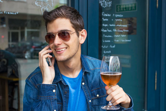 A strange guy in a bar wearing sunglasses, talking on the phone and holding a glass of wine with a smile. A strange guy in a bar wearing sunglasses, talking on the phone and holding a glass of wine with a smile.