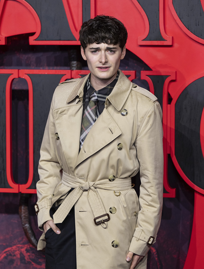 Noah Schnapp at an event, wearing a beige trench coat and patterned tie, relating to Stranger Things star news. Noah Schnapp at an event, wearing a beige trench coat and patterned tie, relating to Stranger Things star news.