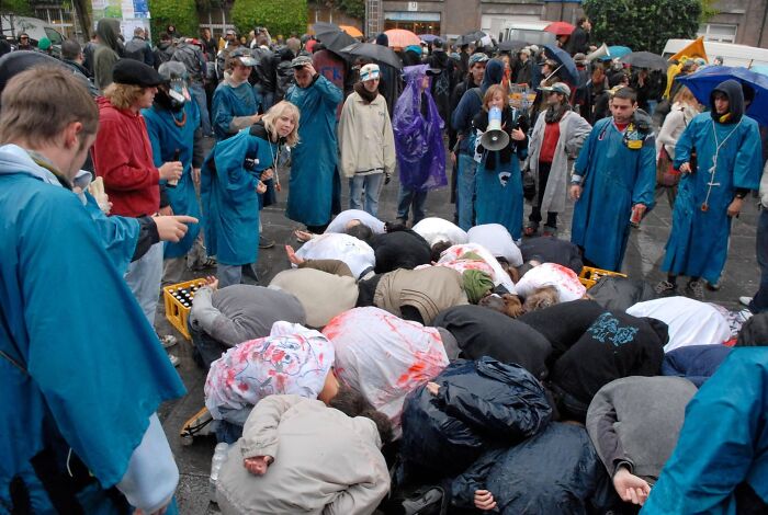 A group of people wearing blue raincoats observing others bent over on the ground during a strange tradition event.