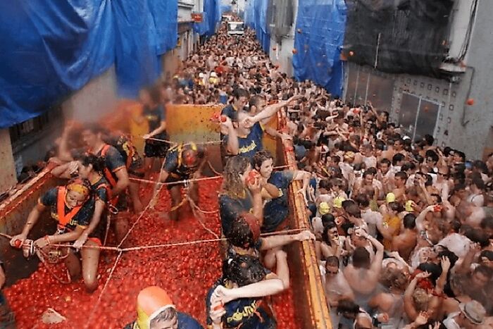 Large crowd participating in a strange tradition involving throwing tomatoes in a narrow street during a festival.