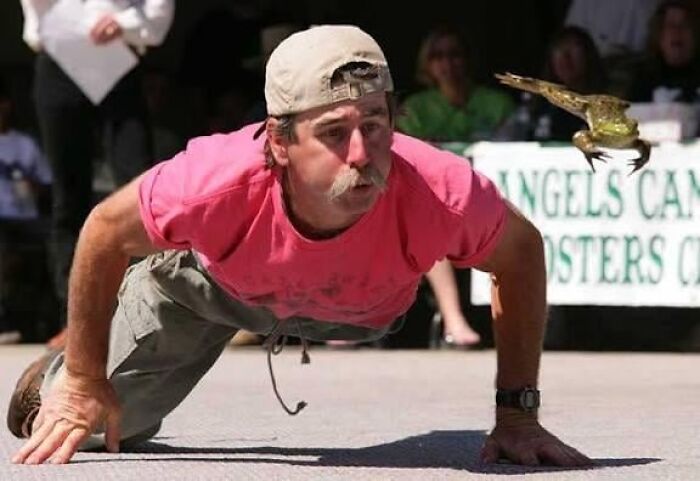 Man in a pink shirt and cap blowing at a flying frog during a strange tradition from around the world event.
