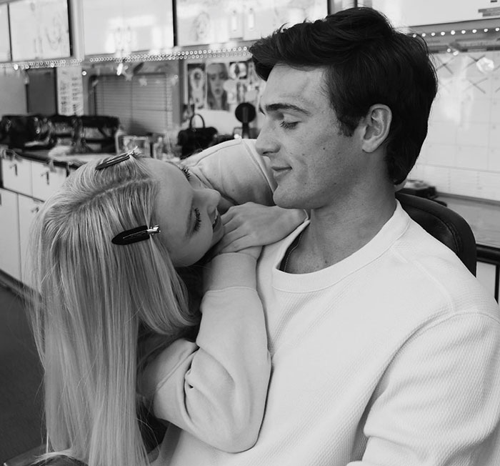 Sydney Sweeney smiling and leaning on a man in a casual indoor setting, portraying an adult star role.