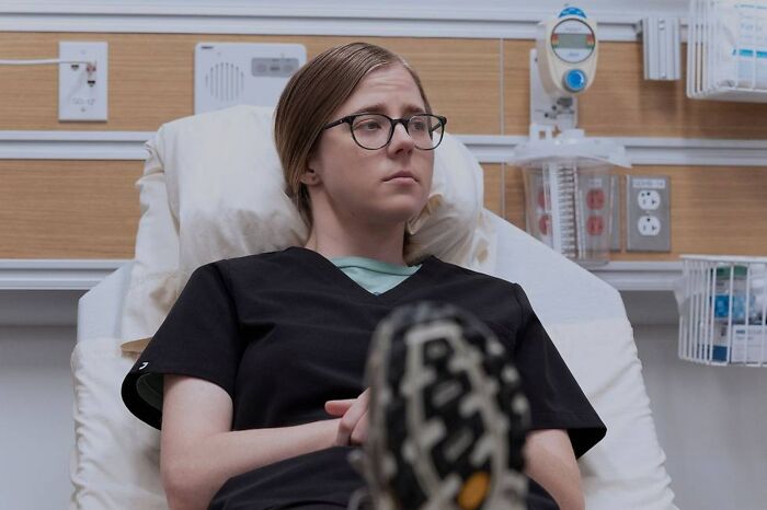 Patient wearing glasses and black scrubs lying in hospital bed, highlighting medical drama disorder portrayal.