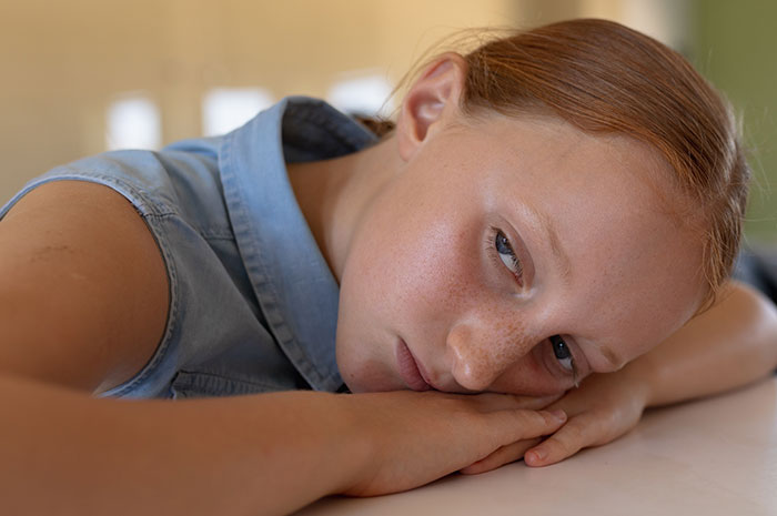 Young girl with red hair resting her head on her arms, looking sad and ignored during an emergency situation. Young girl with red hair resting her head on her arms, looking sad and ignored during an emergency situation.