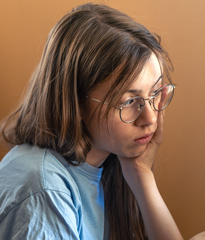 Teen girl with glasses looking thoughtful and upset, reflecting on crushed half-sister&rsquo;s Christmas dreams.