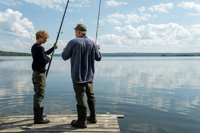 Teen and stepdad fishing together on dock by lake under cloudy sky, highlighting stepdad and teen family tension. Teen and stepdad fishing together on dock by lake under cloudy sky, highlighting stepdad and teen family tension.
