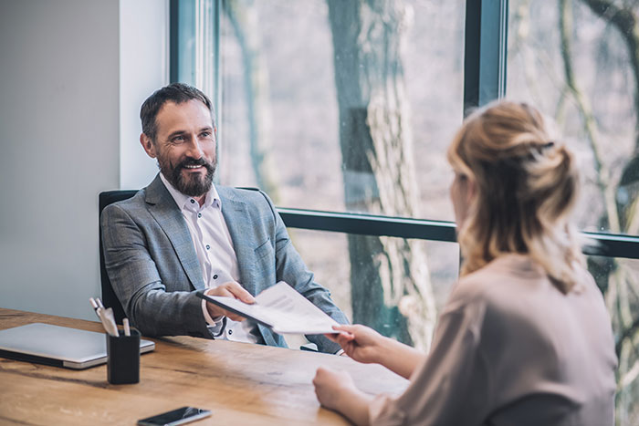 Recruiter in a modern office exchanging resumes with a job candidate during an interview discussing recruitment insights.