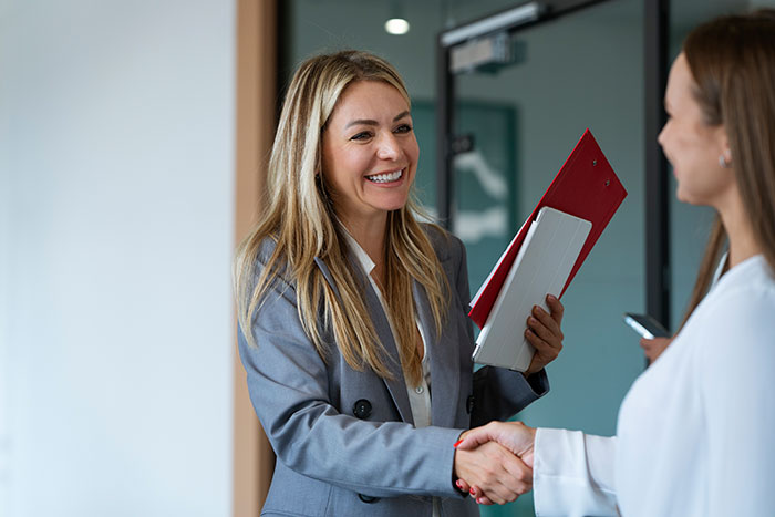 Recruiter in a gray blazer smiling and shaking hands with a job candidate during a professional interview meeting.
