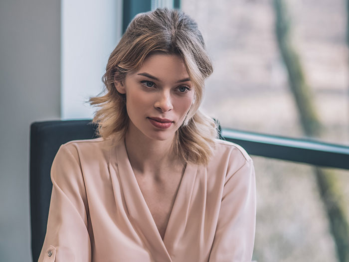 Professional woman in a soft pink blouse during a job interview with recruiters focusing on candidate behavior.