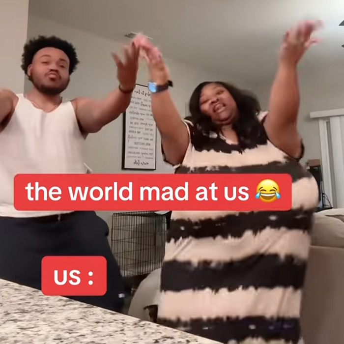 TikTok influencer dancing with friend in living room, text overlay about world being mad at them and their reaction.