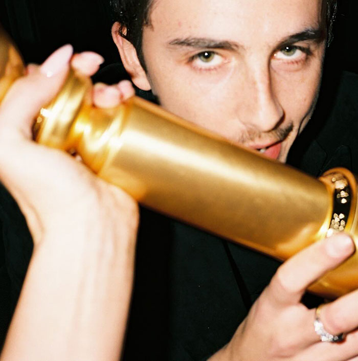 Timothée Chalamet holding a golden object close to his face in a dimly lit setting, sparking backlash online. Timothée Chalamet holding a golden object close to his face in a dimly lit setting, sparking backlash online.