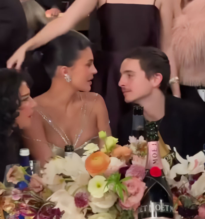 Timothée Chalamet and Kylie Jenner seated at a floral-decorated table during a formal event with drinks nearby. Timothée Chalamet and Kylie Jenner seated at a floral-decorated table during a formal event with drinks nearby.