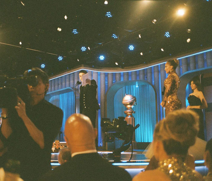 Timoth&eacute;e Chalamet on stage at the Golden Globes with a golden trophy, spotlight, and attendees in the audience.
