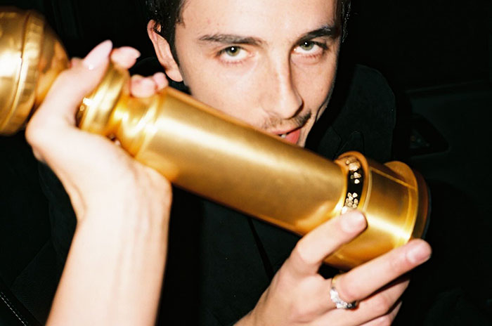 Timothée Chalamet holding a Golden Globe award close to his face in a dimly lit setting after fight news. Timothée Chalamet holding a Golden Globe award close to his face in a dimly lit setting after fight news.