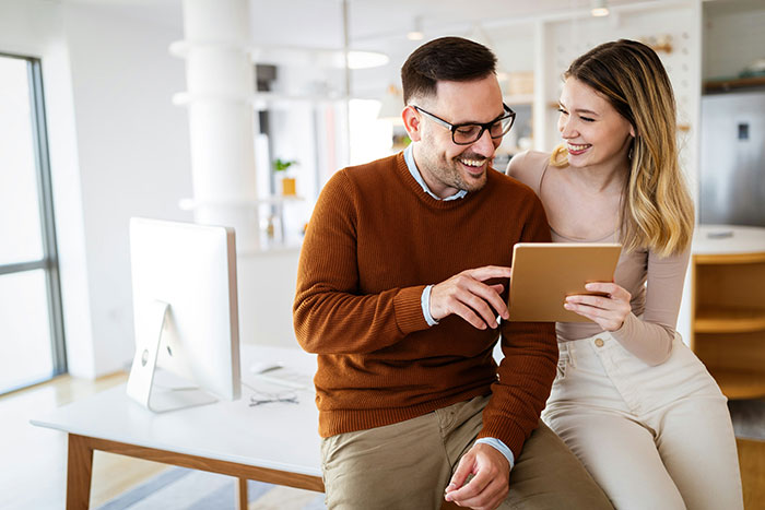 Couple smiling and looking at a tablet in a bright room, illustrating wife’s cosmetic upgrade and relationship tension.