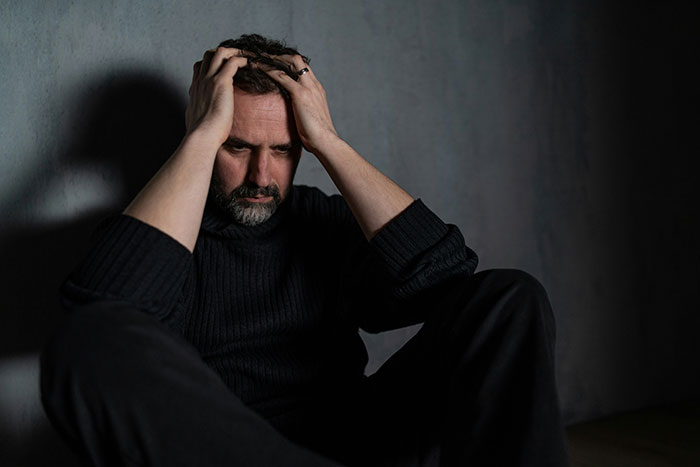 Man in dark sweater sitting against a wall, holding his head in distress, reflecting emotional turmoil from infidelity. Man in dark sweater sitting against a wall, holding his head in distress, reflecting emotional turmoil from infidelity.