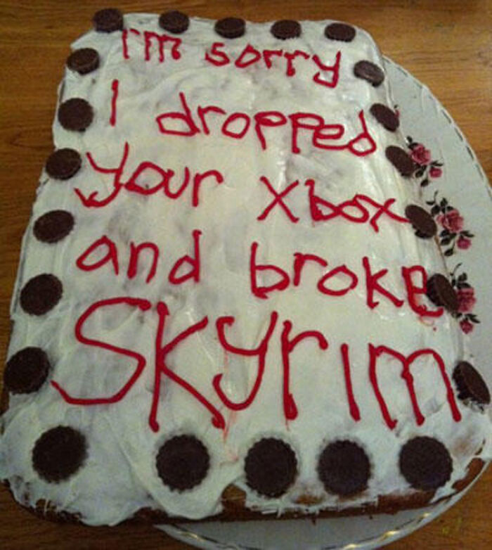 Funny cake with a white frosting and red icing text apologizing for breaking Skyrim, decorated with chocolate cookies on edges.
