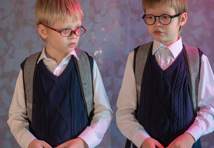 Twin boys in matching school uniforms and glasses, illustrating parent refuses to make twins less similar for school.