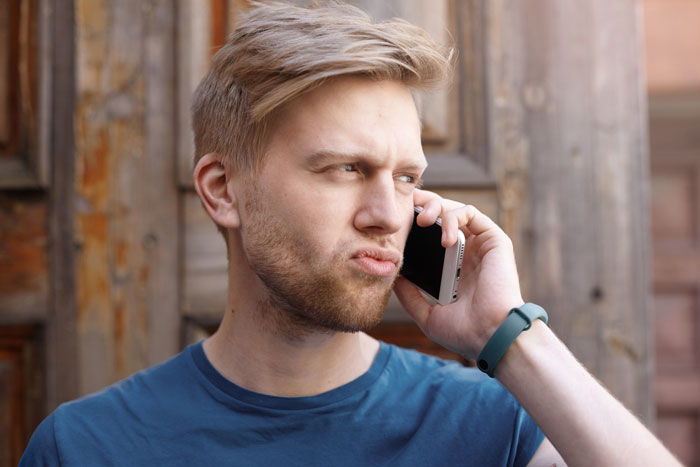 Young man in a blue shirt wearing a wristband, looking frustrated while talking on a smartphone outdoors. Young man in a blue shirt wearing a wristband, looking frustrated while talking on a smartphone outdoors.