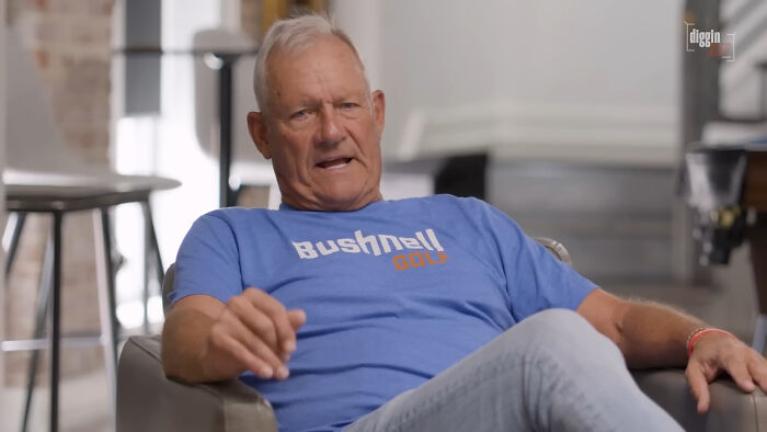 Older man wearing a blue Bushnell Golf shirt sitting in a chair, sharing a story about meeting his idol in real life.
