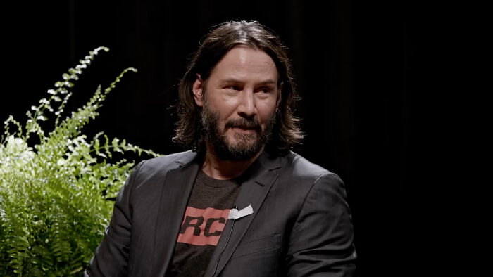 Man with long hair and beard wearing a black blazer and t-shirt, captured during a candid moment meeting an idol in real life.