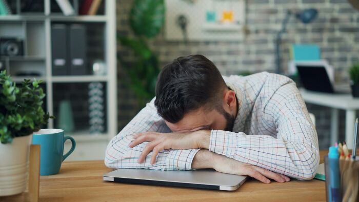 Man exhausted at desk with laptop, representing frustration with worst coworkers in a stressful work environment.